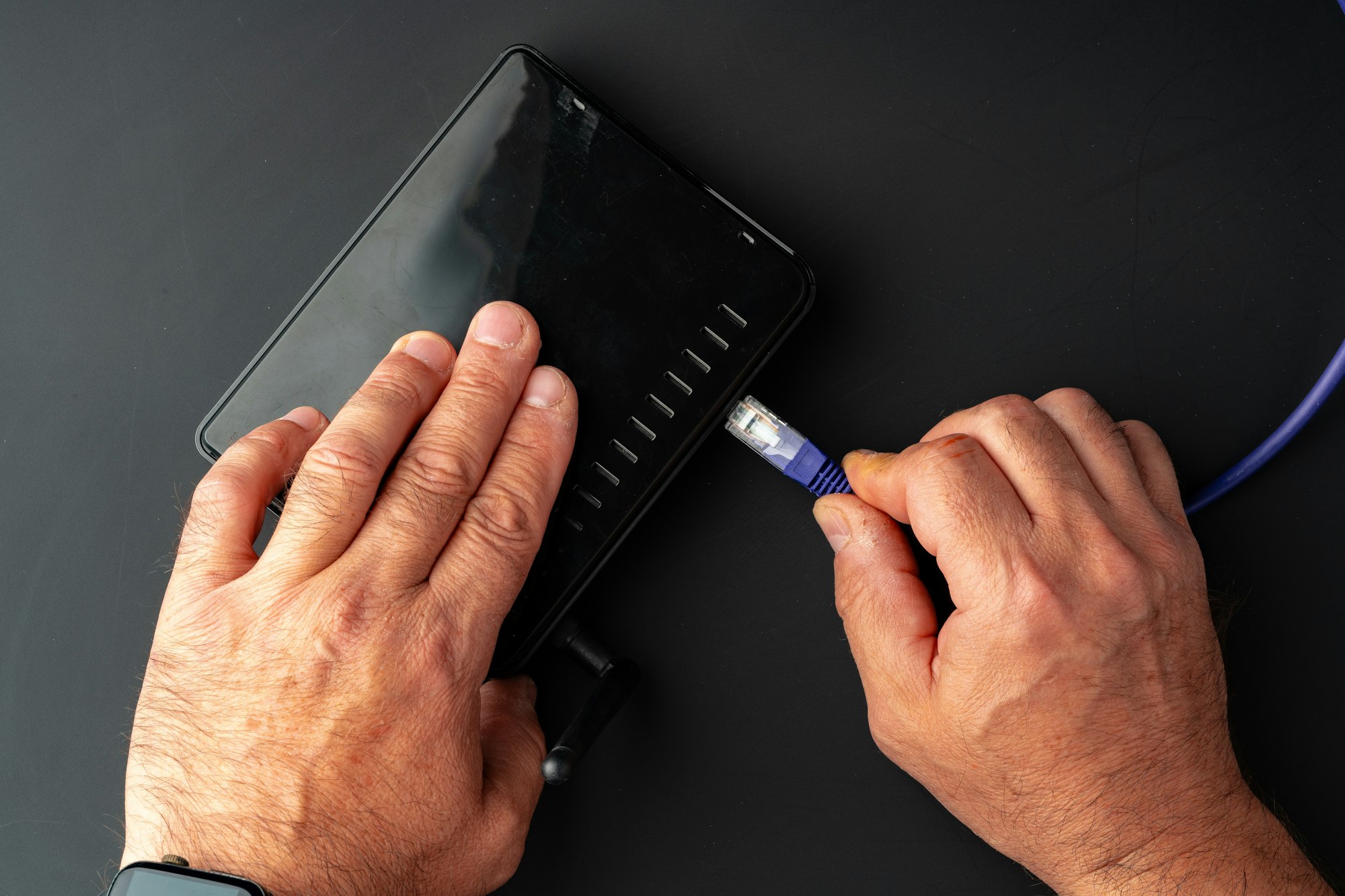 Man's hand plugging internet cable into wifi router