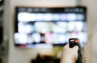 Hand Holding Remote Control Pointing To Tv. Person Watching Smart Television