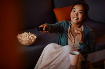 Happy Asian Woman Eating Popcorn While Watching Tv At Home At Night.