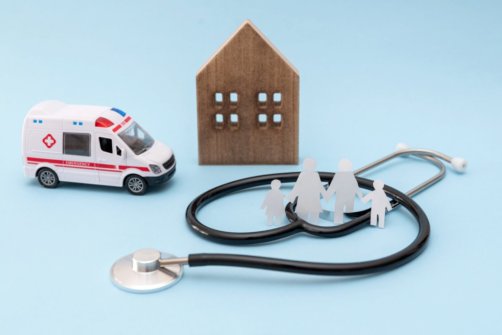 Stethoscope, ambulance toy, wooden house and family on blue background healthcare and emergency